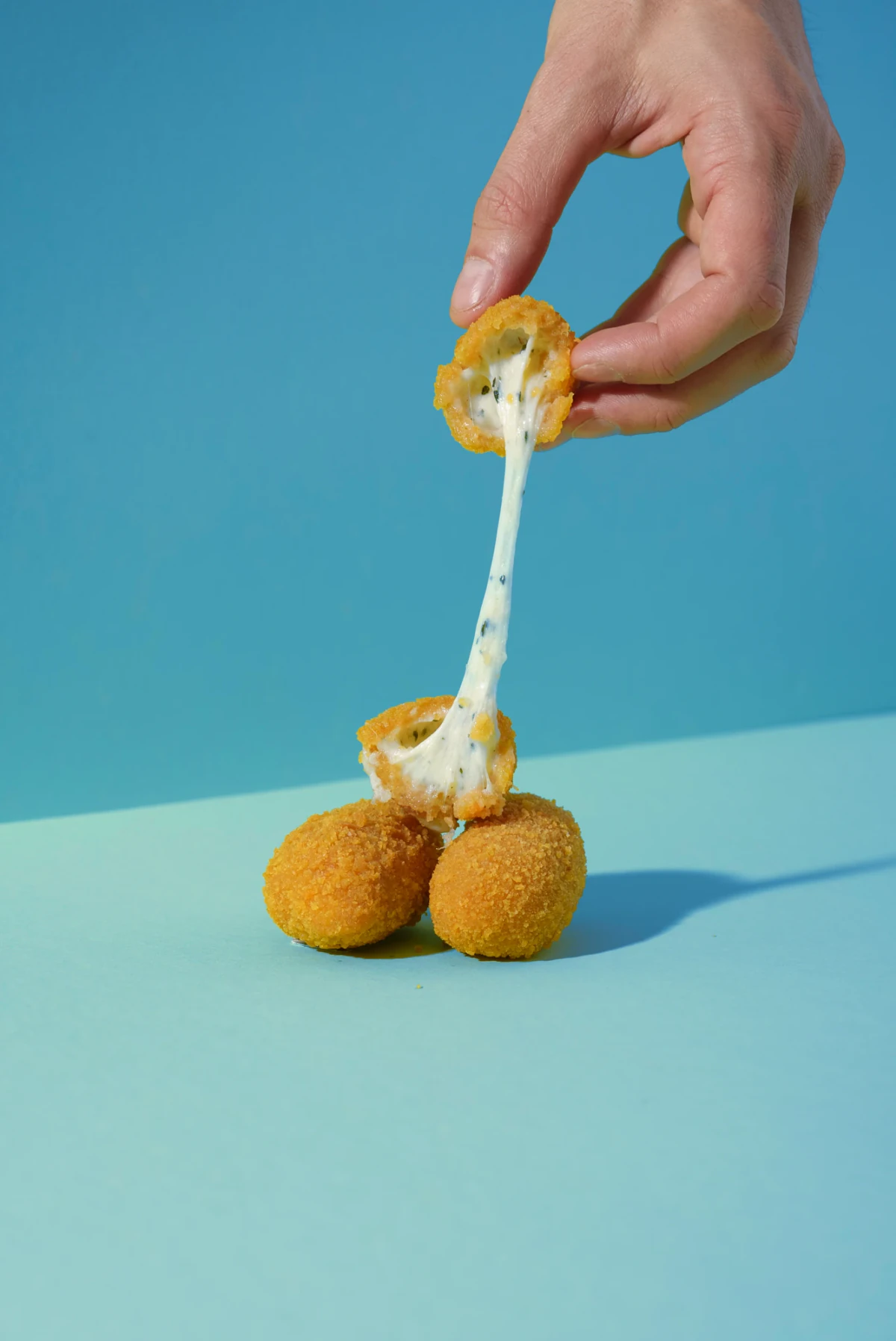 Mozzarellina panata aperta, con cuore di fiordilatte filante su sfondo azzurro