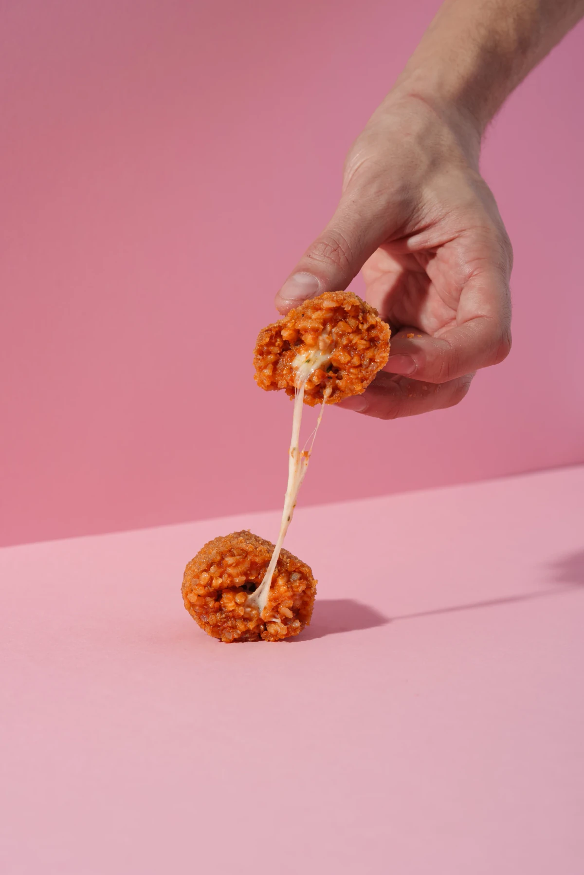100 g Amatriciana supplì, opened to reveal its guanciale and pecorino filling, against a pink background