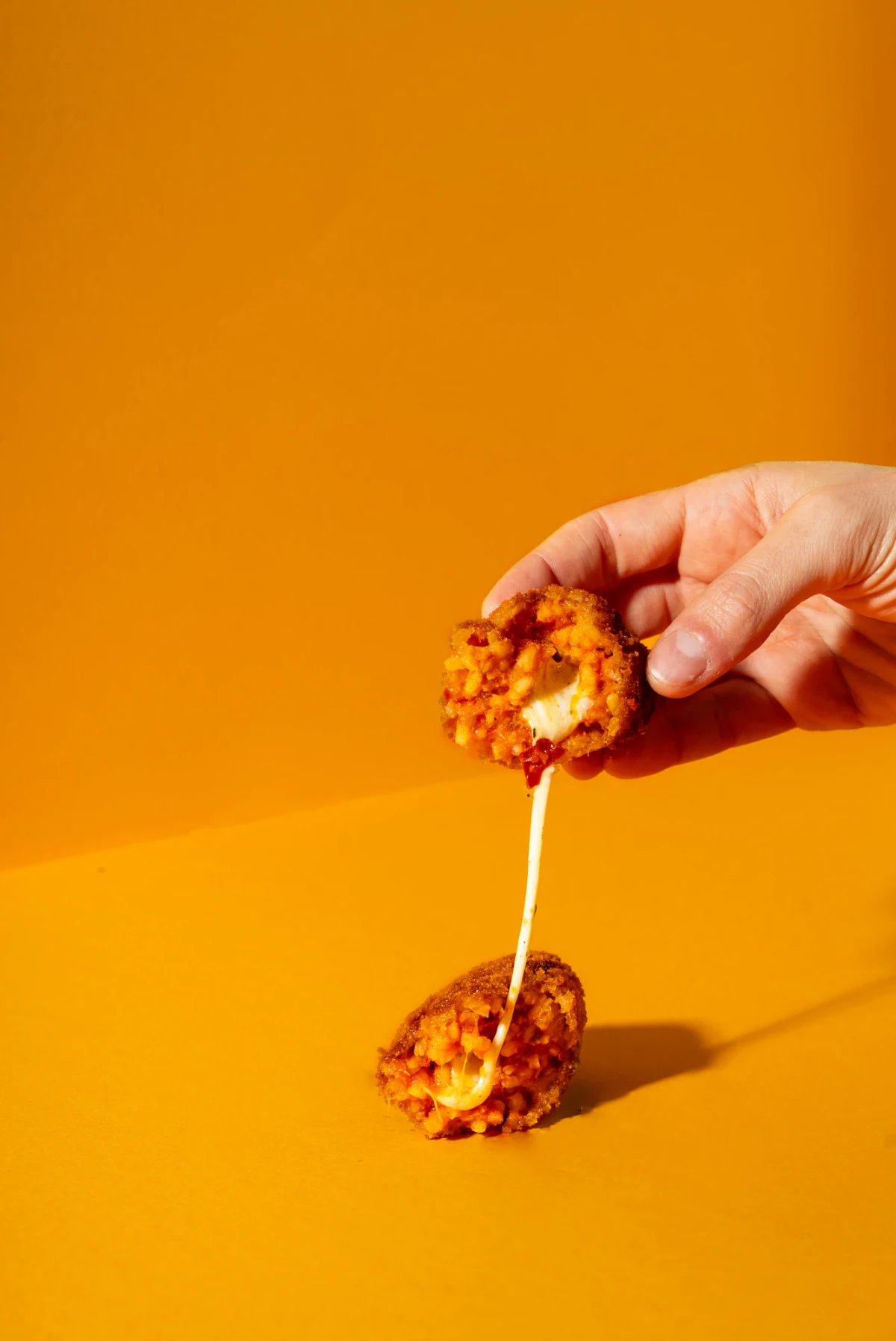 An opened 100 g ’nduja supplì with melted mozzarella on an orange background
