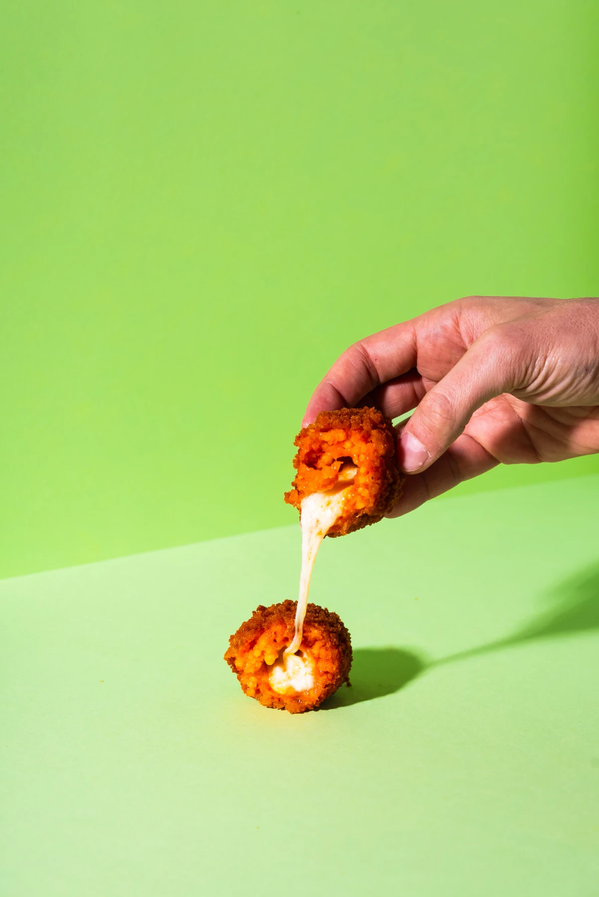 An opened 100 g tomato and basil supplì with melted mozzarella on a green background