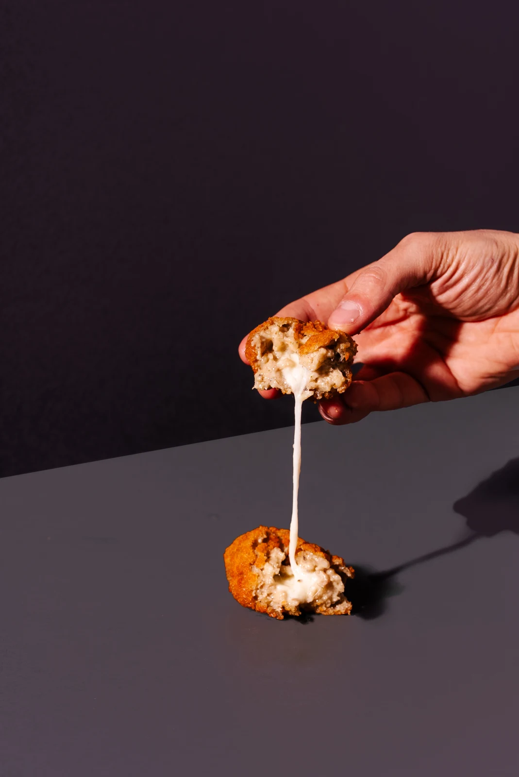 An opened 100 g porcini and truffle supplì with a mushroom filling on a dark background