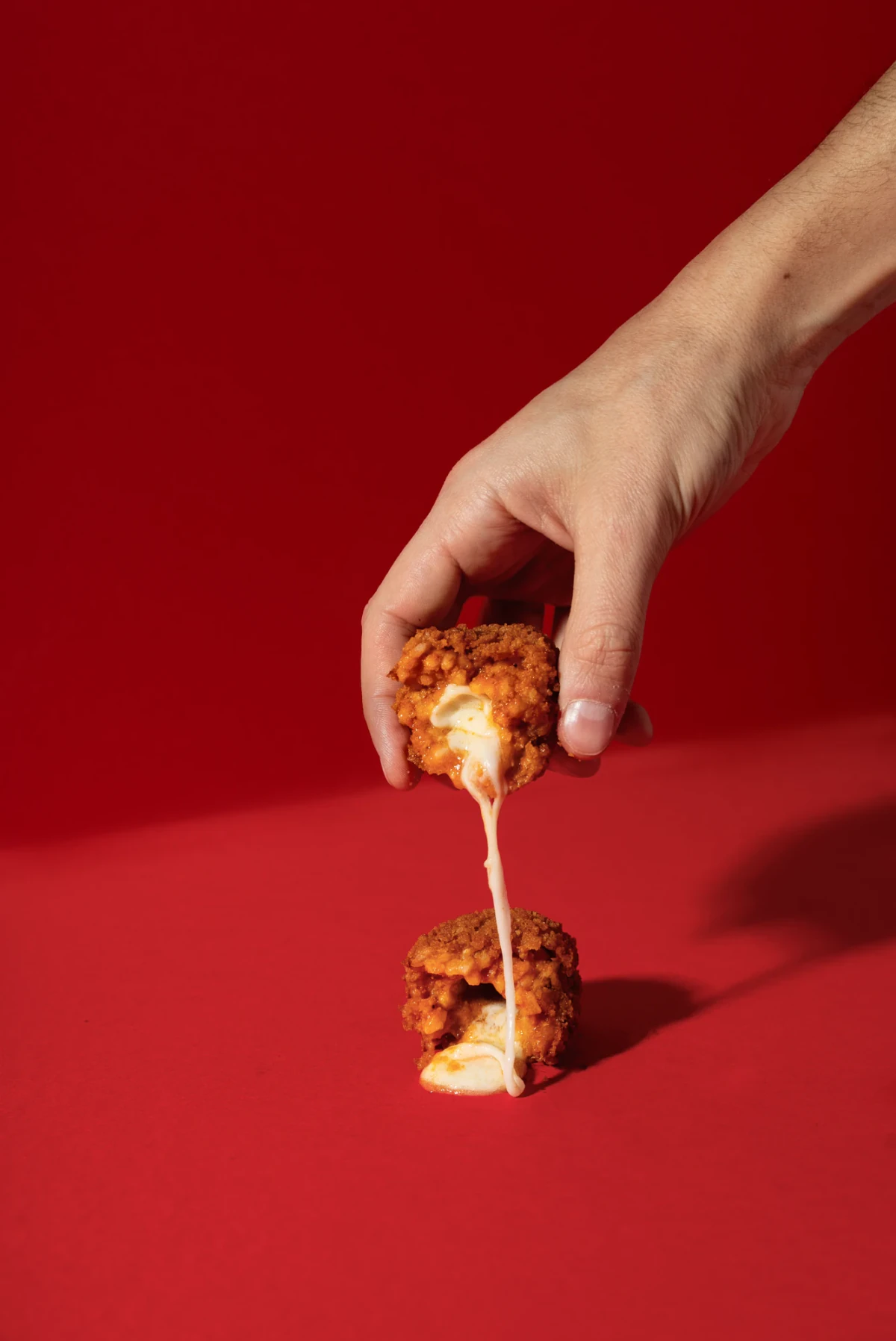 100 g beef ragù supplì, opened to reveal melting mozzarella, against a red background